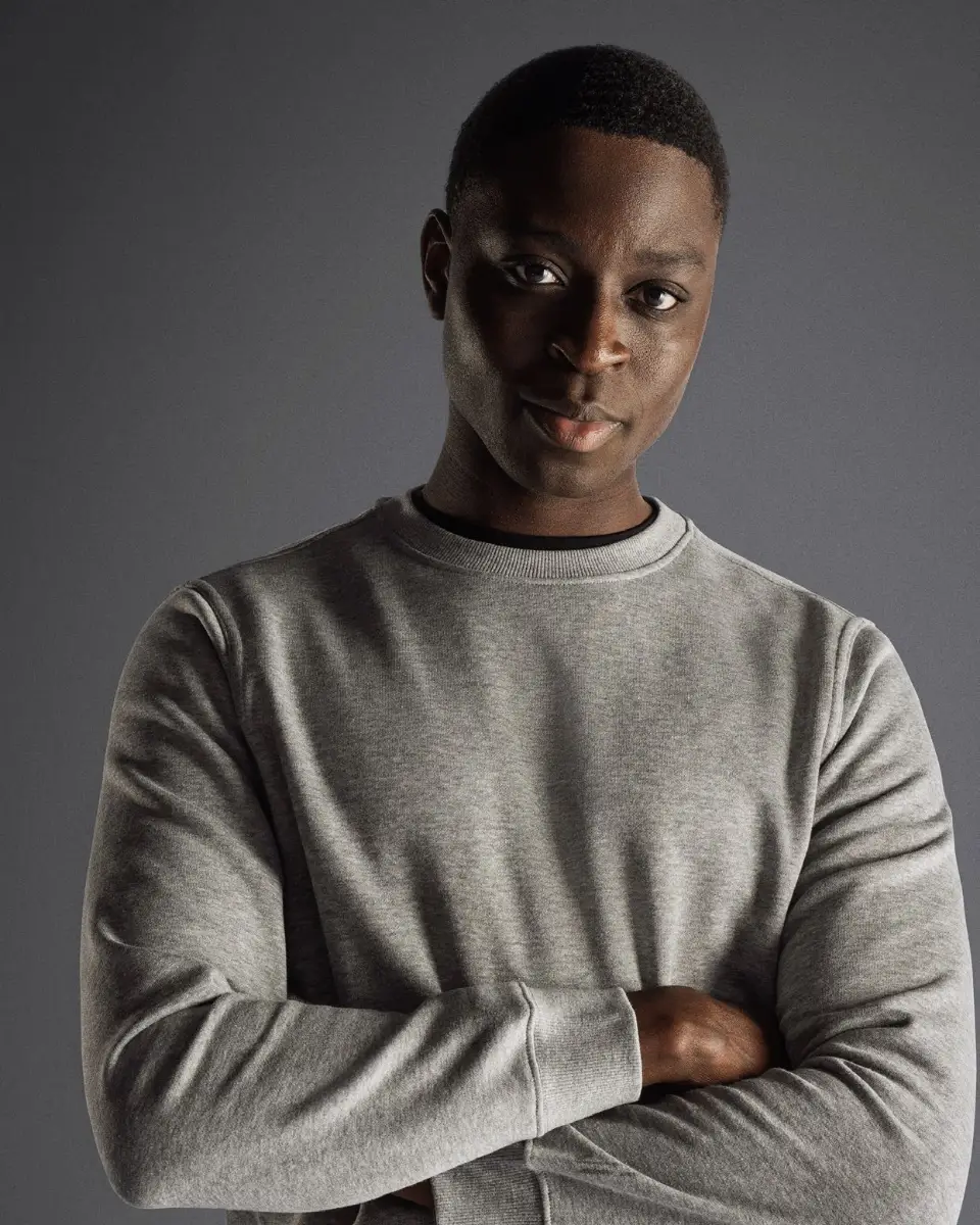 Ung man i grå sweatshirt med armarna i kors mot en mörk bakgrund